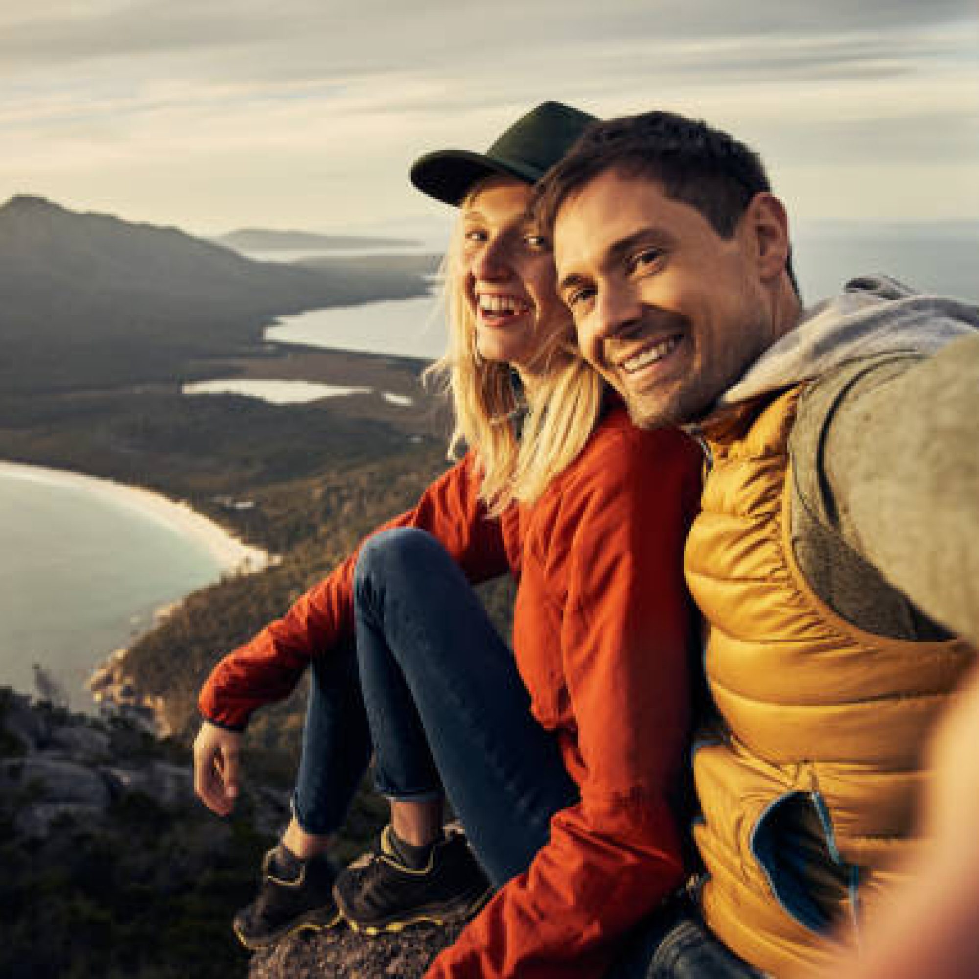 Cropped portrait of an affectionate young couple taking selfies while sitting on a mountain peak